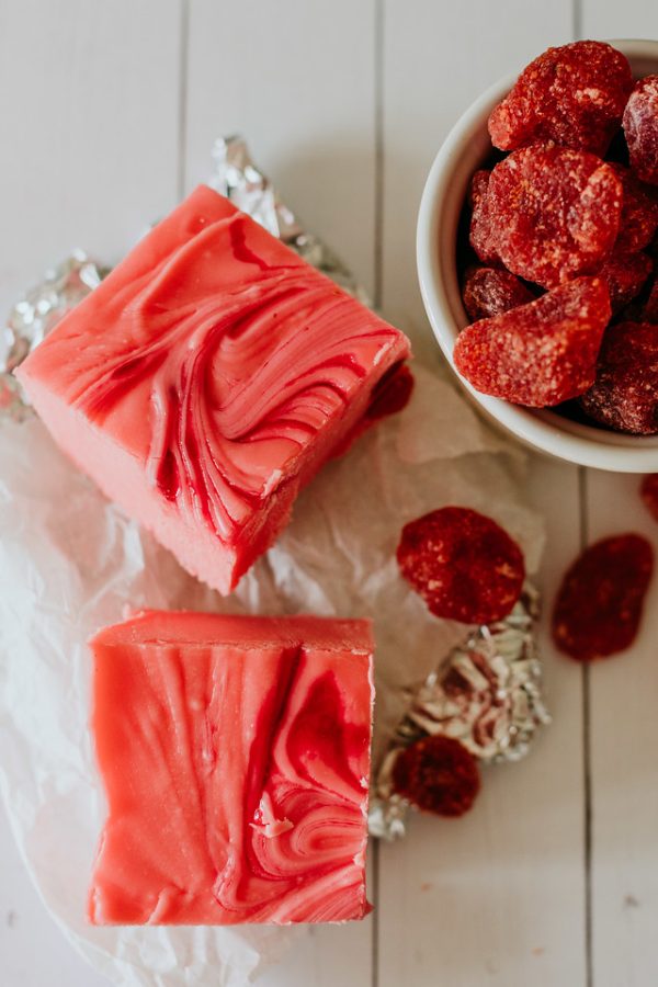 squares of strawberry and cream fudge next to a cup of dried strawberries