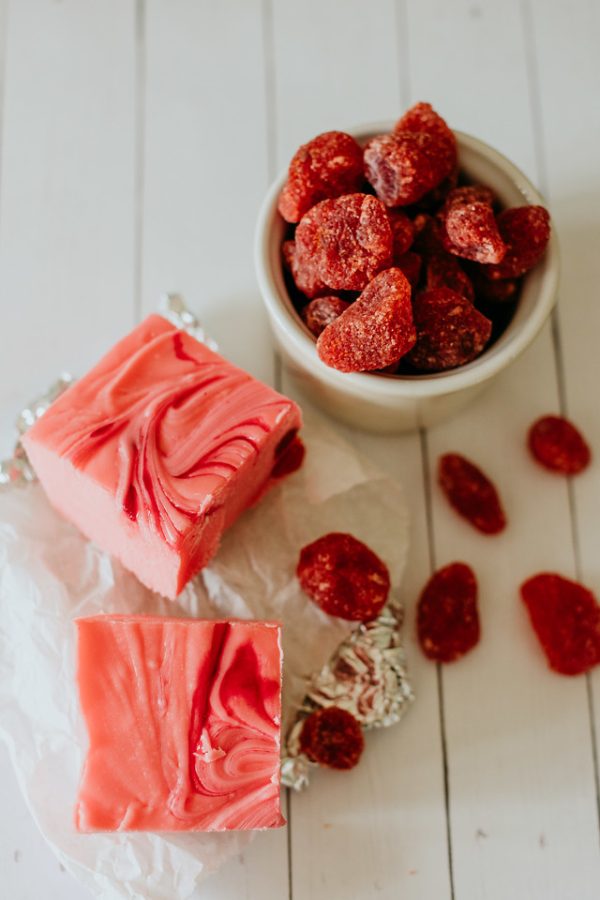 squares of strawberry and cream fudge next to a cup of dried strawberries