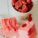 squares of strawberry and cream fudge next to a cup of dried strawberries