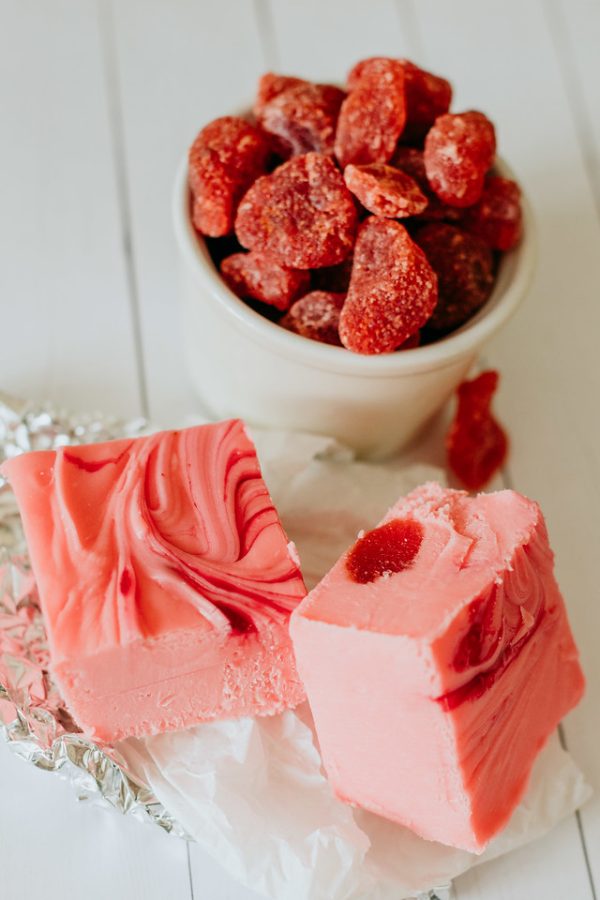 squares of strawberry and cream fudge next to a cup of dried strawberries