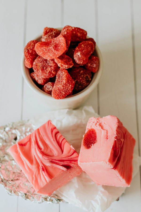 squares of strawberry and cream fudge next to a cup of dried strawberries