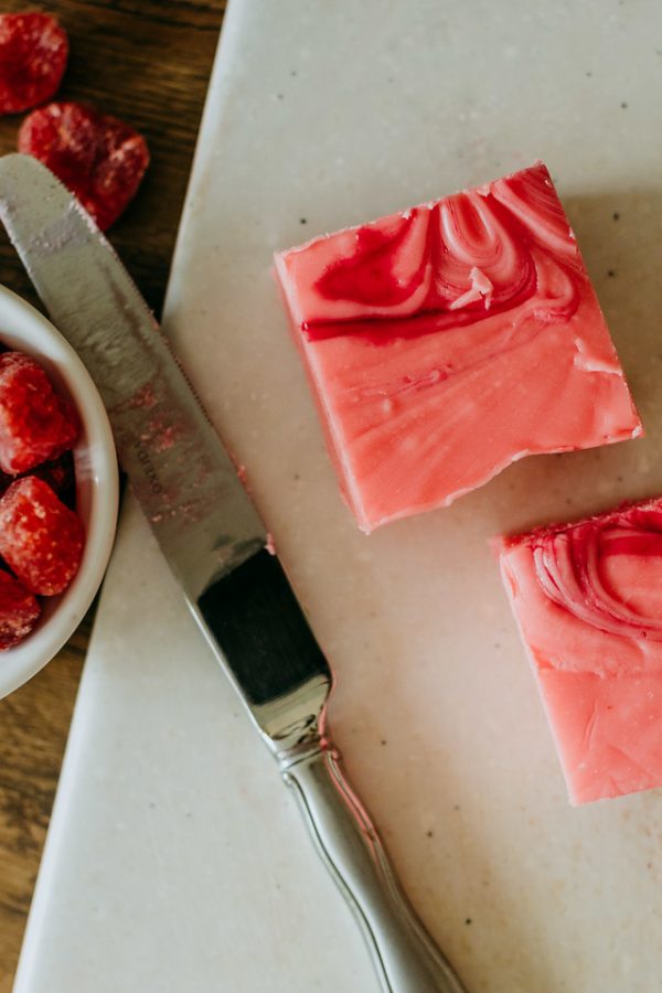 charcuterie board with a knife and squares of strawberry and cream fudge